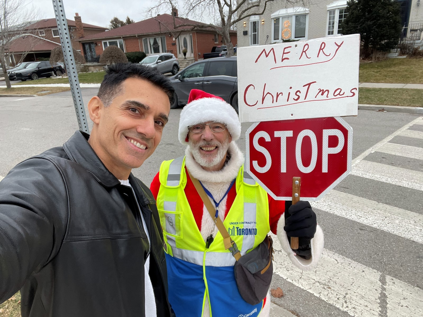 Sinan Erdemir with a Toronto school crossing guard beside a hand-painted Merry Christmas stop sign