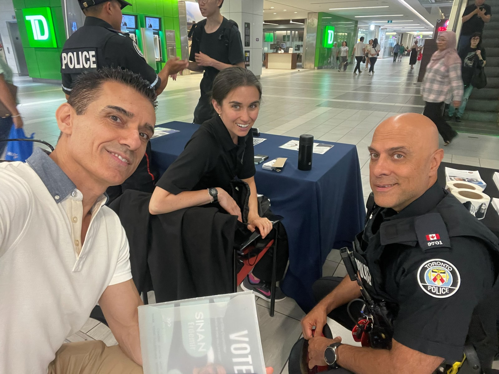 Sinan Erdemir at a campaign outreach table with a volunteer and a Toronto police officer